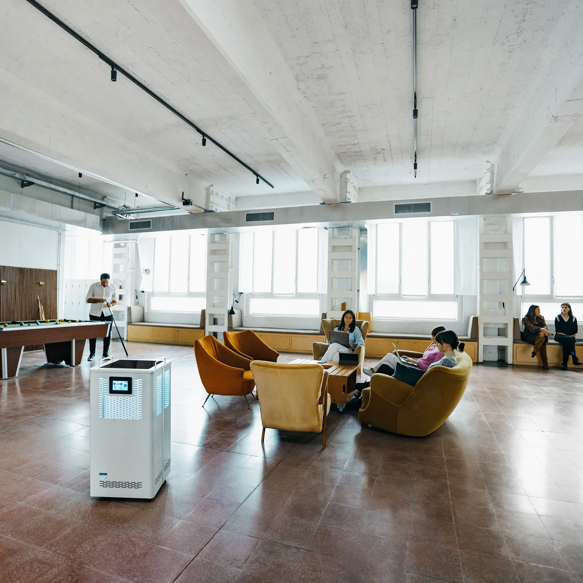 Spazio di coworking a Milano con grandi finestre: persone al lavoro sulle poltrone e un purificatore d’aria in primo piano