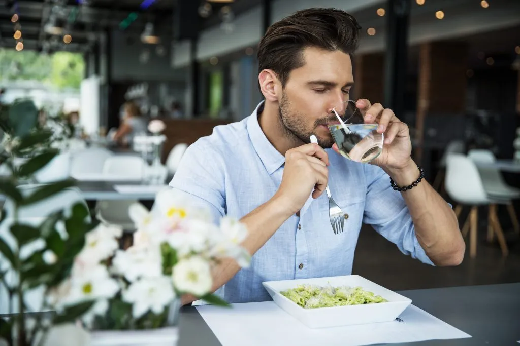 Cliente al tavolo di un ristorante che beve un bicchiere d’acqua durante il pranzo