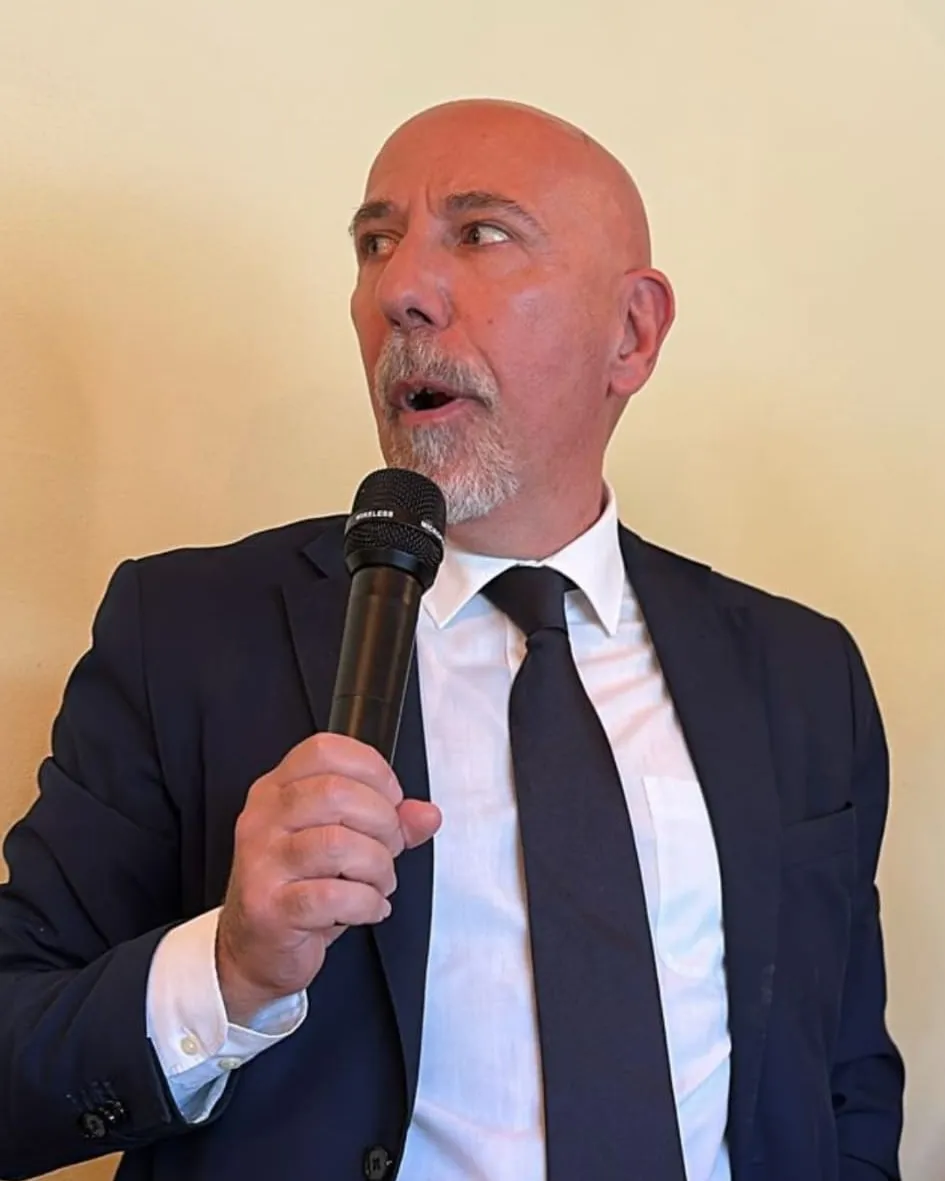 Giuliano Santi in giacca e cravatta mentre parla al microfono durante un incontro